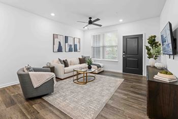 A living room with a grey armchair, a white sofa, a coffee table, and a TV on the wall.